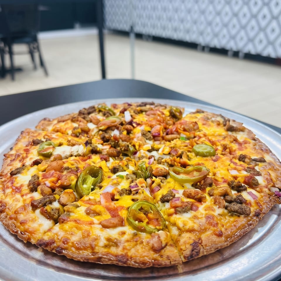A whole pizza with cheese, meat, and jalapeños on a metal tray in a restaurant setting.