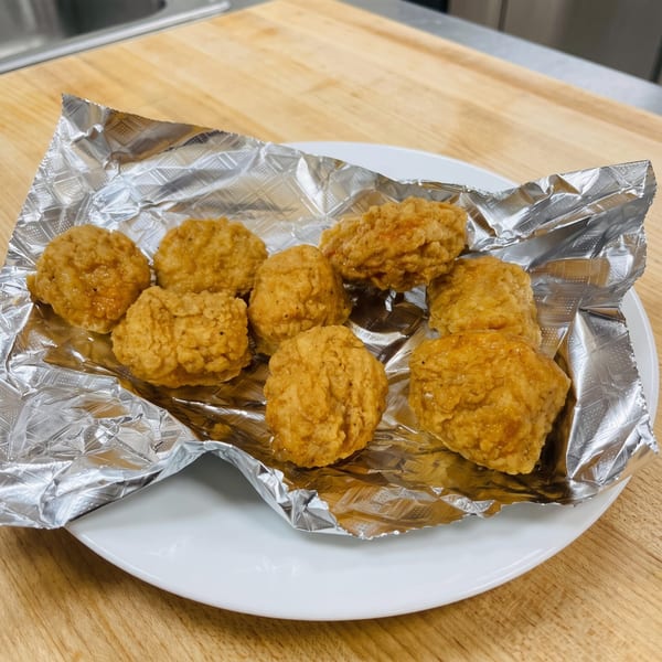 Golden-brown fried chicken nuggets on aluminum foil, served on a white plate on a wooden table.
