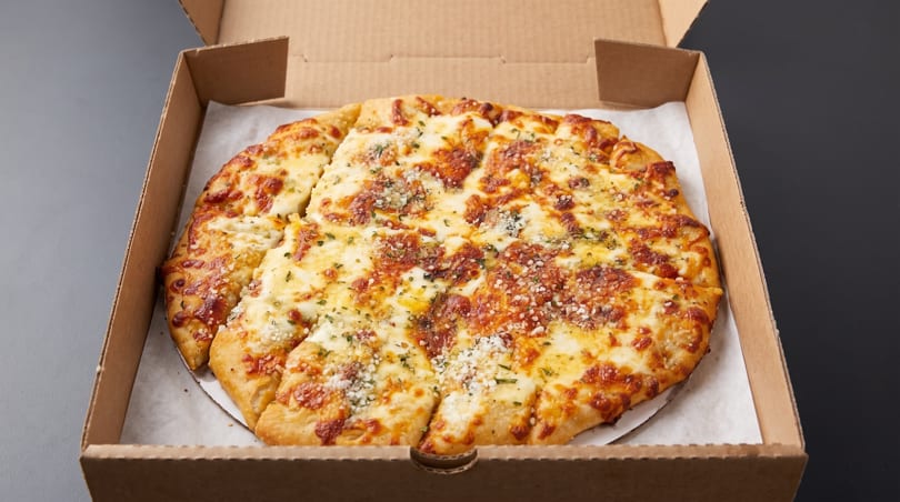 Cheesy garlic bread, cut into slices, in a brown cardboard pizza box.