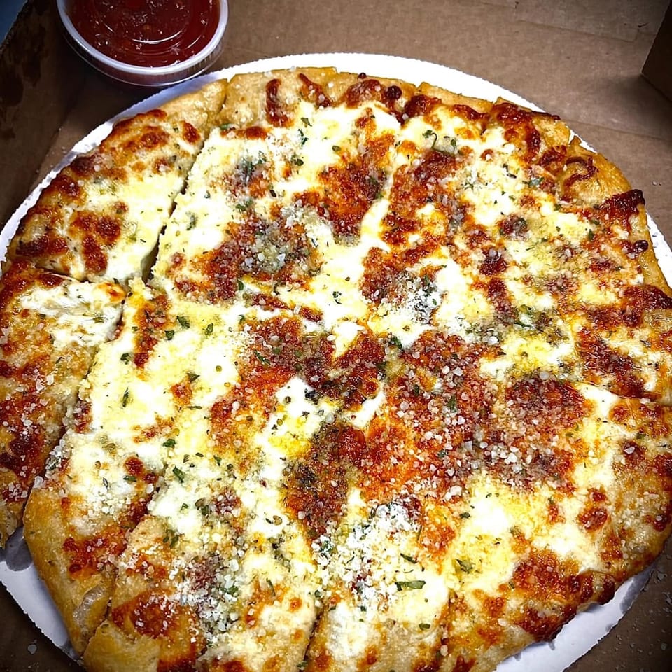 A freshly baked, sliced garlic knot pizza with melted cheese and herbs, served with a side of marinara sauce.