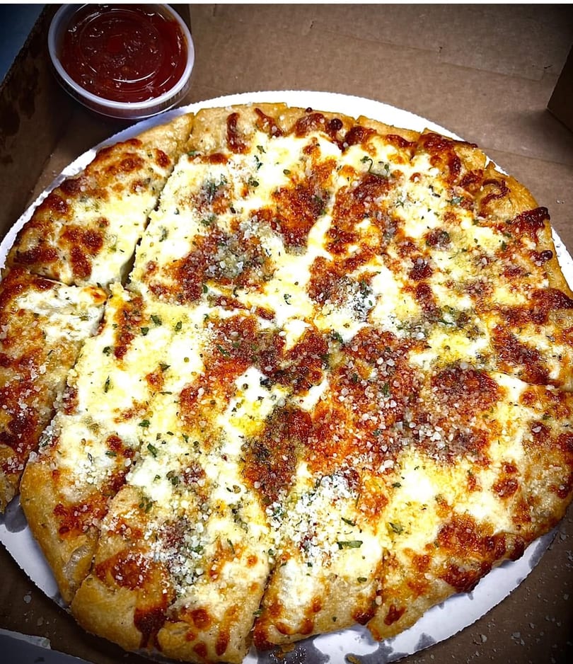 A freshly baked, sliced garlic knot pizza with melted cheese and herbs, served with a side of marinara sauce.