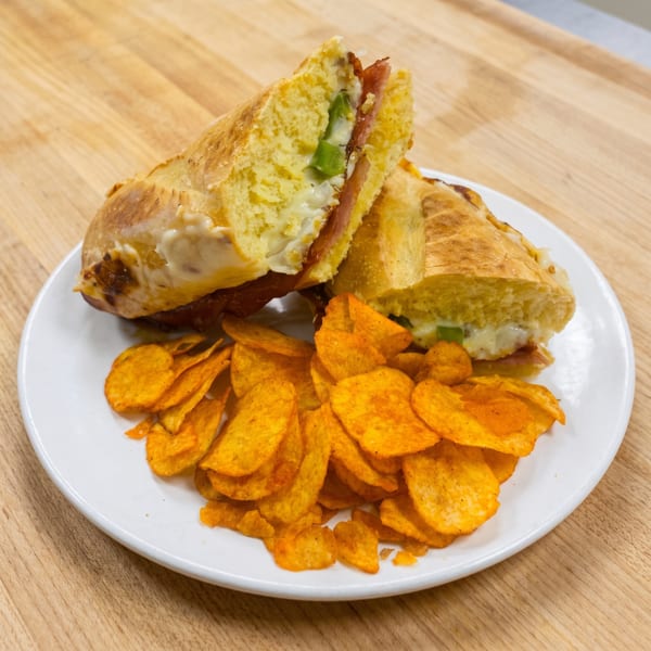 A toasted sandwich with melted cheese, green peppers, and meat, served with a side of chips.